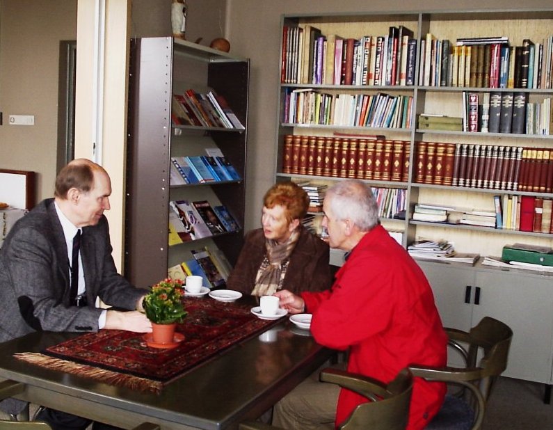 Pater Frank Dirven in samenspraak met twee mensen in de bibliotheek